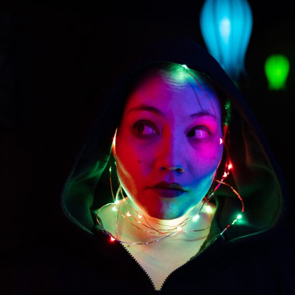 Decorative - Background for text.
Face of a person in a hooded sweatshirt. Her face lit up by small string lights of varied color.